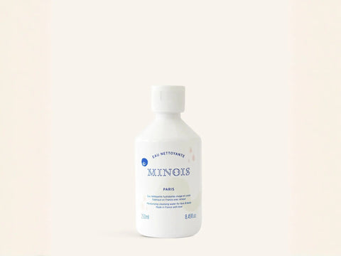 Eau nettoyante Minois Paris pour visage et corps, nettoyage sans rinçage, flacon transparent avec logo blanc.